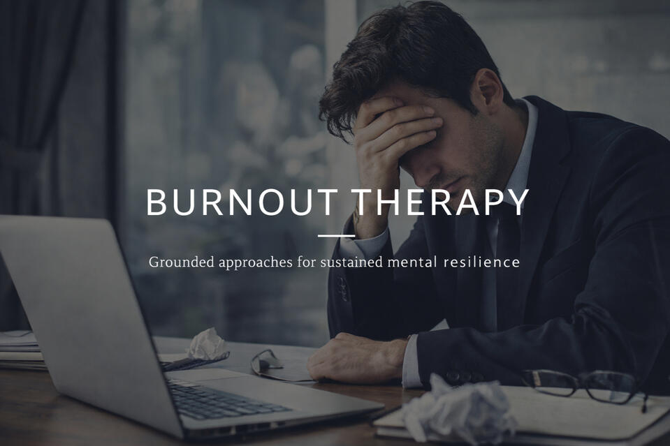 This image shows a man who seems to be a business professional at his work desk who is holding his head in his hands sitting at a computer looking like he is very stressed out from burnout, and may want to consider burnout therapy to help improve mental he